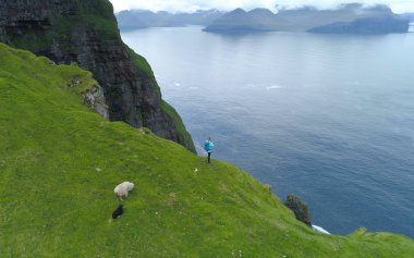 Hava: deniz fotoğrafını çekmek bir uçurumun kenarından kadın bir uzun yürüyüşe çıkan kimse yukarıda uçan. Profesyonel fotoğrafçı Faroe Adaları çimenli dağlarda hiking doğal kırsal fotoğrafını çekmek.