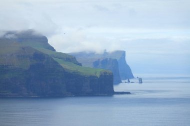 Hava: sakin okyanus ve pitoresk Seaside Faroe Adaları muhteşem bir adacık siyah kayalıklarla doğru uçan. Engebeli İskandinav kıyı bulutlu gün manzarası.