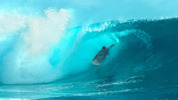 CLOSE UP: Cool male surfboarder rides and drags his hand along a beautiful glassy wave heading towards the exotic coast of Tahiti. Cheerful young sportsman finishes carving a perfect barrel ocean wave