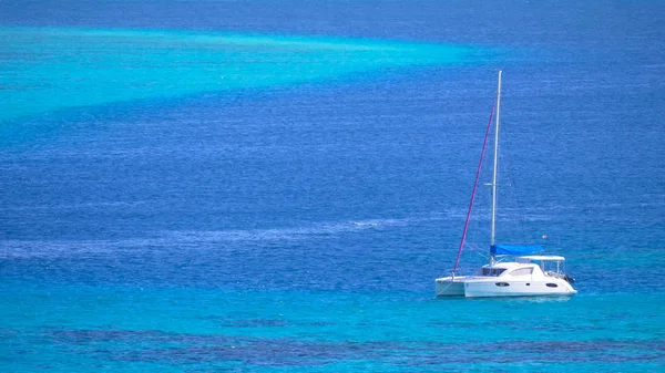 White sailboat resting in the tranquil turquoise ocean water on a sunny summer day in the Pacific. Cool shot of yacht sailing in the calm sea. Luxury vessel cruising around the tropical seaside.