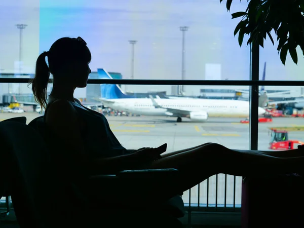 无名的年轻女子拿着手机 看着一个大的国际机场的跑道 无法辨认的女性旅行者耐心地等待她漫长的航班回家 — 图库照片