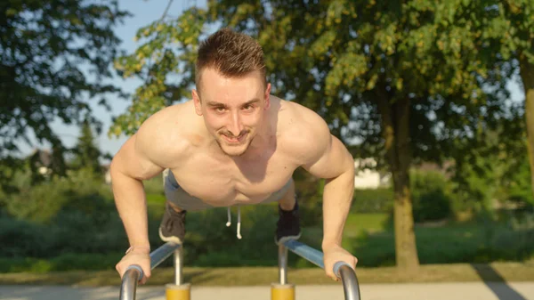 Portre: Kaslı adam mı push up paralel çubuklarında harika açık spor salonunda. Basın yapan beyaz adam gülümseyen güneşli doğada ups. Genç atletik erkek eğitim dışında sıcak yaz havalarda.