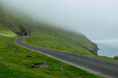 Boş doğal sahil yolu doğru karanlık tünel bulutlu bir günde Faroe Adaları içinde çalışır. Çimenli İskandinav kırsal çalışan bir boş Asfalt izi okyanustan güzel görünümü.