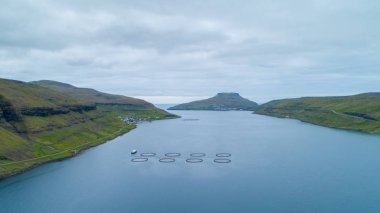 Hava: pitoresk Faroe Adaları'uzak kıyı kenti yakınlarında büyük bir balık çiftliği yukarıda uçan. Doğal yeşil dağların küçük sakin İskandinav balıkçı köyü kuşatır. Güzel engebeli doğa.