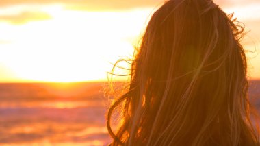 Lens Flare, kopya alanı, yakın Up: güzel akşam güneşi ve plaja doğru sıçramasına küçük deniz dalgaları bakarak tanınmaz halde genç kadın fotoğrafçı. Kız ve günbatımı sinematik görünümünü.