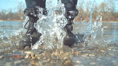 CLOSE UP: Unrecognizable playful woman jumping in the shallow water of a calm crystal clear stream. Cheerful girl having fun splashing the refreshing pond water with her feet in black hiking boots.
