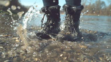 Yakın: kristal berraklığında su onun bulanık siyah çizmeler ferahlatıcı stream etrafında atlama tanınmaz oynak kızın ayak etrafında su sıçramalarına. Sinematik çekim stomping kadının ayaklarının göle.
