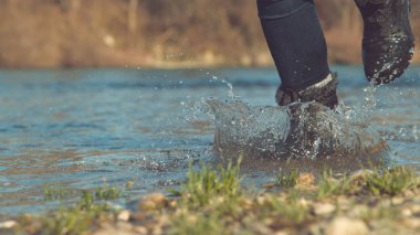 Düşük Açı: Camsı nehir suyu sonbahar güneşinde parlarken tanınmaz enerjik kız sakin dere boyunca koşar. Güneşli açık havada zevk tanınmayan oyuncu kadın Sinematik çekim.