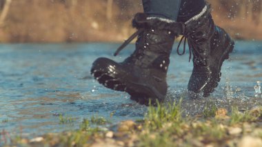 düşük açı: Onu su geçirmez siyah çizmeler sığ göl etrafında koşarak sıcak sonbahar gününde zevk eğlenceli kız. Onu kürklü yürüyüş botları sakin dere de koşu tanınmaz kadın.
