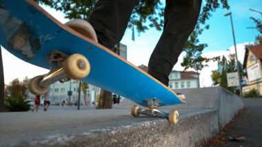 CLOSE UP, DOF: Unrecognizable young skateboarder in black pants and sneakers grinds a concrete ledge in the urban park. Cool skater tail grinding a ledge in a scenic park in the green city streets.