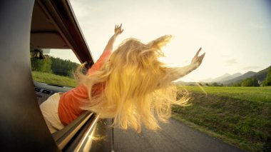 Yakın: güneşli yaz akşamı ile pitoresk kırsal manzara seyir arabadan uzanan bilinmeyen sarışın saçlı kadın. Sabah araba yolculuğu sırasında eğlenmek tanınmaz kız.