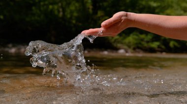 CLOSE UP: Unknown young woman's hand splashes the crystal clear river water on a sunny day in the mountains. Unrecognizable female hiker freshens up by scooping up a handful of water from the creek.