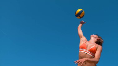 Low Angle, Close Up: Bir plaj voleybolu maçı sırasında bikinili, beyaz bir kadın topu servis ediyor. Atletik bayan voleybol oyuncusu havaya zıplar ve maç sayısı için topu ezer..