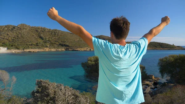 Yakın: Tanınmayan genç erkek turist güzel sahilinde bakarken kollarını outstretches. Neşeli adam kollarını zaferle bir İtalyan Adası'nın doğal bakış açısı ulaştıktan sonra yükseltir.