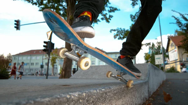 CLOSE UP DOF: Young skateboarder tail grinds a concrete ledge in skatepark. Unrecognizable skater dude wearing cannabis socks doing cool tricks on his skateboard on a beautiful autumn day in the city.