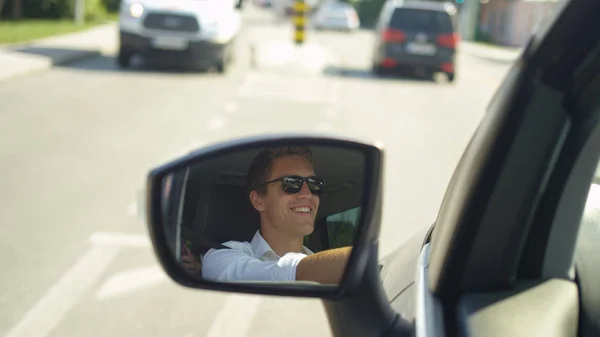 クローズ アップ 被写し界深度 幸せな若い白人男は晴れた日に町を通って通勤します 町を通って風光明媚なドライブを楽しむ陽気な男性ドライバーの車のサイドビュー ミラーでクールな反射 — ストック写真