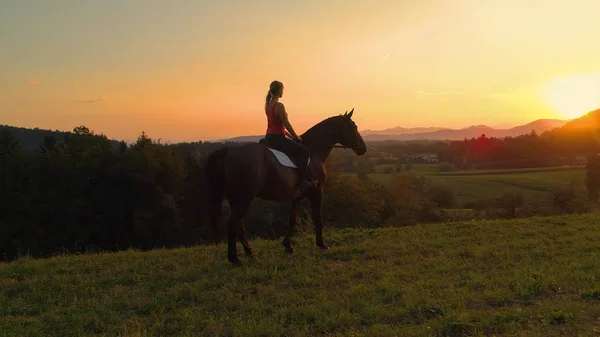 彼女の馬の上に座って 日の出を見て未知の若い女の子の背後にある空中 レンズフレア 彼女の馬および絵のようなスロベニア語の夜の風景を観察することで認識できない女性が座っています — ストック写真