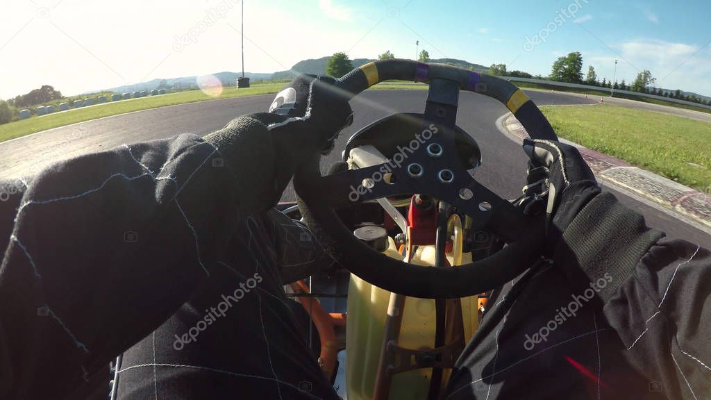 POV, LENS FLARE: Having fun racing a go kart along a bumpy asphalt racetrack on a sunny day. Cool shot of arms and legs driving a fast go-cart around the raceway during a cool time trial competition.