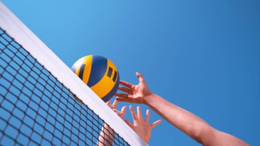 LOW ANGLE, CLOSE UP: Unrecognizable female volleyball player spikes the ball past the block set up by her opponent in a beach volleyball tournament. Cinematic shot of a volleyball smash at the net.