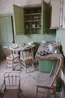 Dust gathering on the chairs and table in the dining room in an abandoned house in a former mining town. Walking through the decaying rooms of an antique wooden house from the California gold rush. clipart