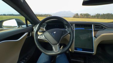 Özerk Tesla araba, Mart 2018 - Pov: genç kadın ile pastoral kırsal bir güneşli bahar gününde sürüş. Kadın kendini bir direksiyon arabada kendisi kırsal rota boyunca navigasyona commuting.
