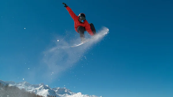 彼は空気を通って飛ぶ壮大なグラブ トリックをしながら雪の証跡を残し男性スノーボーダーの素晴らしいアクション ショット プロのスポーツ選手がアルプスでスノーボードの息をのむショット — ストック写真