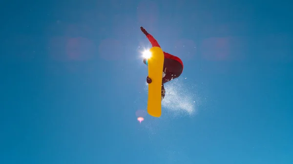 ボトムアップ レンズフレア 空気中の高いトリックをしながら 明るい冬の太陽光によって照らされたプロの男性スノーボーダー 完璧な冬の日に休日のスノーボードのアスレチックマン — ストック写真