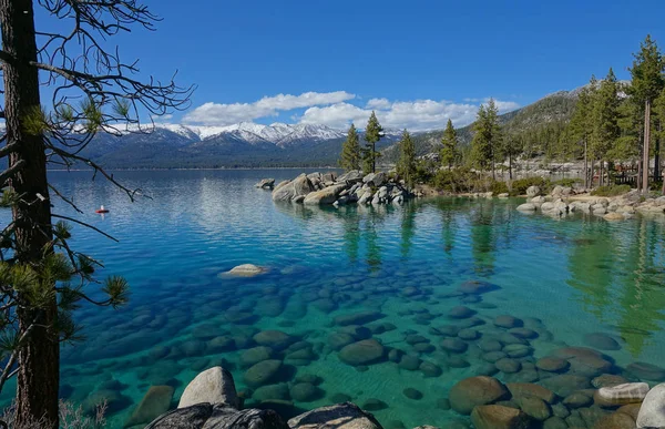 Breathtaking view of the snowy mountains overlooking the emerald colored lake in the scenic American wilderness. Warm autumn sun shines on the idyllic national park in USA. Spectacular Tahoe Lake.