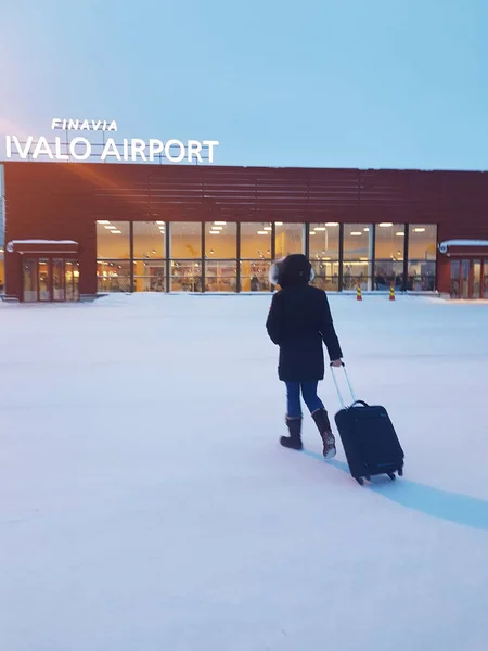 穿着冬季夹克的年轻女子无法辨认 走向伊瓦洛机场 女性旅行者携带她的旅行袋 她走在一个小机场的入口在斯堪的纳维亚的风景 — 图库照片