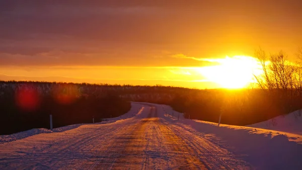 風光明媚なノルウェーの牧歌的な雪に覆われた田舎を通って実行している空の雪に覆われた道路上空中 レンズフレア 雪の風景に輝く黄金の朝木漏れ日の空気からの眺望 — ストック写真