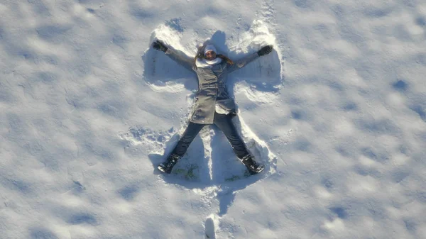 自上而下 微笑的年轻白种人妇女躺在深雪和一个雪天 快乐的女孩有乐趣 通过在新鲜的粉末雪玩重温她的童年记忆 — 图库照片
