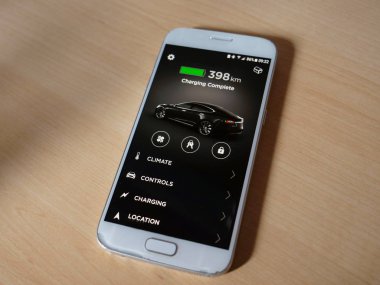 Tesla özerk araba, Mart 2018 - kadar yakın: beyaz smartphone Tesla araba sinyalizasyon ahşap masanın üzerinde yatan tam doludur. Cool cep telefonu uygulaması futuristik araba pil denetleyen.