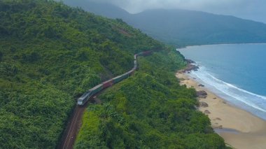 Drone: pitoresk Hai Van Pass Vietnam boyunca tren acele yukarıda uçan. Uzak Asya adanın kapsayan yoğun tropik orman geçerken tren muhteşem manzarası. Güzel kıyı.