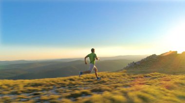 Anteni, Lens Flare: Uçan çimenli tepeden gün batımında Sprint atletik genç erkeğin arkasında. Slovenya manzaralı dağlarında bir güneşli yaz akşamı çalıştıran uygun erkek sinema ateş düştü.