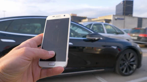 自主汽车 2018年3月 Dof 不明身份者用很酷的手机应用程序控制高科技特斯拉汽车 拿着手机召唤自驾游车辆的人 — 图库照片