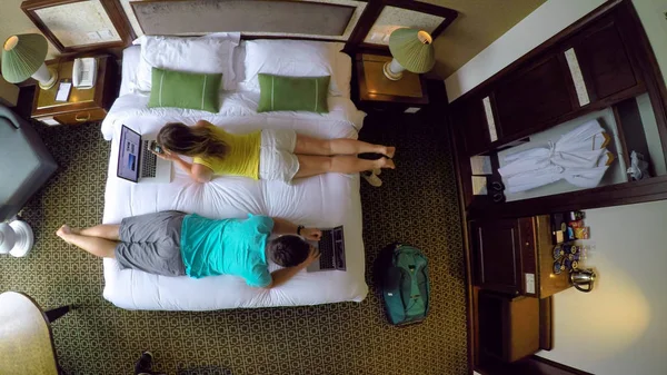 自上而下 年轻夫妇躺在酒店房间的大床上工作 男性和女性数字游牧民族打字和工作在他们的笔记本电脑上 而在越南的有趣的假期 — 图库照片