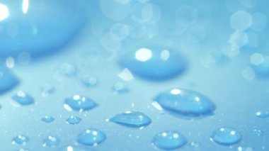 Dof, Makro, Close Up: Islaçık mavi bir otomobilin çatısının yüzeyinde parlayan farklı su damlacıkları. Su damlalarını mavi yüzeye yansıtır. Hafif yağış sonrası ıslak araba çatısında parlak sıvı kabarcıklar