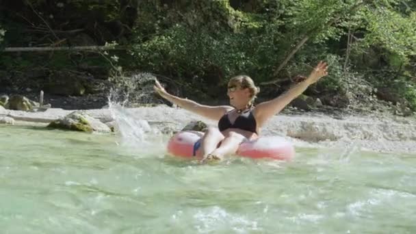 MOVIMIENTO Lento Mujer joven salpicando agua mientras flota en una rosquilla inflable — Vídeos de Stock