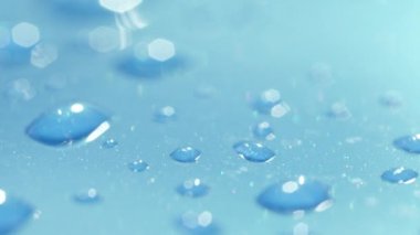 Dof, Makro, Close Up: Açık mavi otomobilin çatısının yüzeyinde parlayan farklı büyüklükteki yağmur damlaları. Su damlalarını mavi yüzeye yansıtır. Hafif duş sonra ıslak araba çatısında parlak şeffaf kabarcıklar.