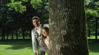 Yavaş Hareket Gülümseyen çift ağacın arkasından peek ve hayranlıkla birbirlerinin gözlerine bakmak. Aşık erkek ve kadın eğlenceli bir ağaç tarafından poz. Karı koca açık havada zevk anlamlı bir görünüm paylaşmak