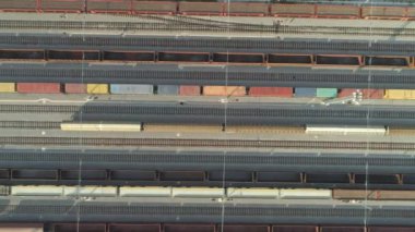 Havadan Yukarıdan Aşağıya: Güneşli bir günde yük konteynırlarıyla endüstriyel demiryolu istasyonundan ayrılan yüklü yük tren vagonlarının üzerinde uçmak. Endüstriyel demiryolu terminalinde boş demiryolları ve konteyner trenleri.