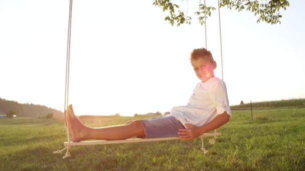 슬로우 클로즈업 행복한 소년은 일몰에 스윙에 편안한 아이는 저녁에 스윙에 — 비디오