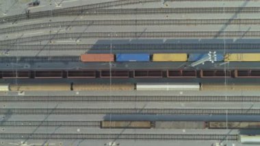 Havadan Yukarıdan Aşağıya: Güneşli bir günde endüstriyel demiryolu istasyonunda navlun konteynerlerini geçen boş yük treninin üzerinde uçmak. Endüstriyel demiryolu terminalinde boş demiryolları ve ihracat konteyner trenleri.