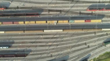 Havadan Yukarıdan Aşağıya: Güneşli bir günde yük konteynırlarıyla endüstriyel demiryolu istasyonundan ayrılan yüklü yük tren vagonlarının üzerinde uçmak. Endüstriyel demiryolu terminalinde boş demiryolları ve konteyner trenleri.