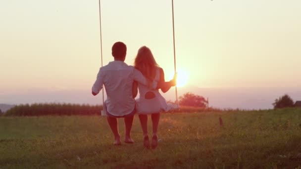 スローモーション ロマンチックな若々しいカップルは 大きな木の下で揺れ 夕日を見て日付 自然の中の地平線を見渡す夏の夜にスイングに平和の瞬間を共有する幸せなパートナー — ストック動画