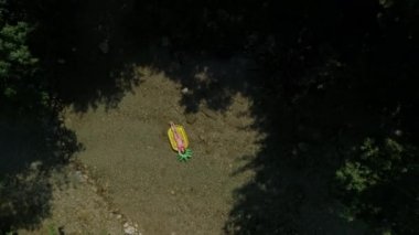 Aerial Top Down: Yakındaki nehirde ananas yüzen yatan güzel kadın. Riverside tatilde tasasız turist onu tan üzerinde çalışıyor. Genç kadın yerel derede çarpıcı doğada rahatlatıcı.