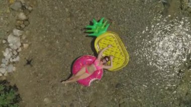 Hava Topdown Genç kadın sıcak günde yerel nehirde rahatlatıcı 2 yüzen karşısında yatıyor. Ananas ve çörek floatie üzerinde gevşeme Laidback esmer. Nehir kenarında tatilin tadını çıkaran güzel turist