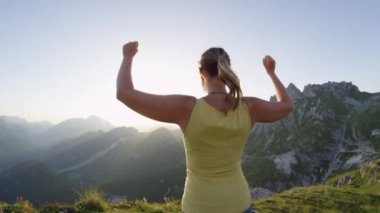 Slow Motion Mutlu kadın altın gün batımında kayalık dağın tepesinde muzaffer bir şekilde kollarını kaldırıyor. Gün doğumunda dağın zirvesine ulaşırken yürüyüş kız kollarını uzamış. Genç trekker günlük hedefe ulaşma