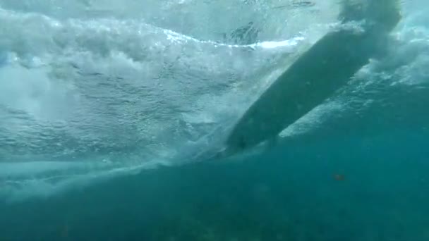スローモーション水中 白いサーフボードの滑空とターコイズブルーの海を彫刻し 波紋を作ります 熱帯の島の近くの澄んだ水の中でサーフボードで急旋回をする認識できないサーファー — ストック動画
