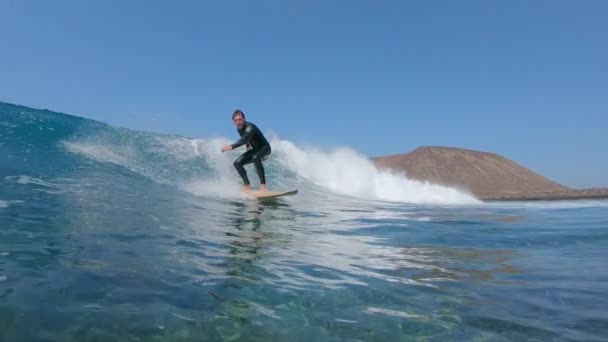スローモーション水中 休暇サーフィン海の波にサーファーの男をフィット 火山島の近くで素晴らしい大波に乗ってサーファー 透明な水に浸す前にサーフボード上の男性の映画撮影 — ストック動画
